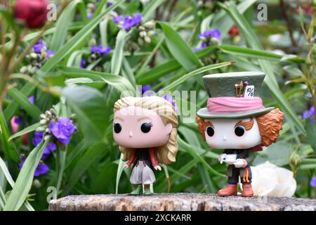 Funko Pop Actionfiguren von Mad Hatter und Alice im Wunderland aus dem beliebten Tim Burton Fantasy-Film. Blumen, fabelhafter Garten, Holzstumpf. Stockfoto