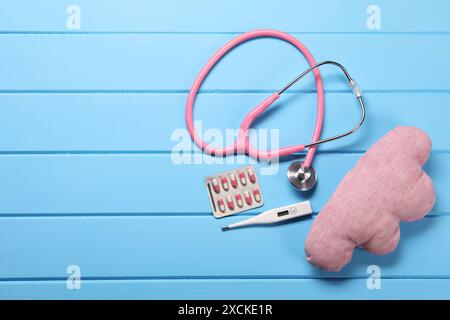 Kissen, Stethoskop, Thermometer und Pillen auf hellblauem hölzernem Hintergrund, flache Lage. Leerzeichen für Text Stockfoto