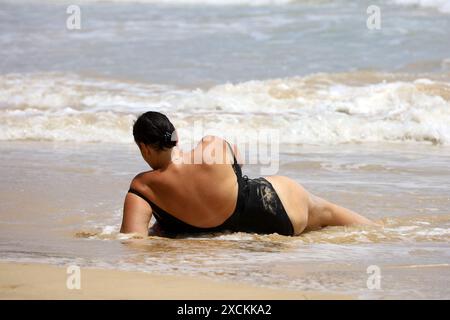 Frau im schwarzen Badeanzug sonnt sich an einem Sandstrand auf Meereswellen Hintergrund Stockfoto