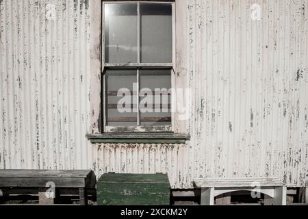 Altes doppelhängendes Fenster in einer Außenwand aus Wellblech mit grünem Kasten und Sitzbänken. Stockfoto