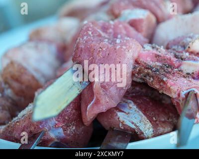 Nahaufnahme von rohen, gewürzten Fleischstücken auf Metallspießen, bereit für die Zubereitung des georgischen Gerichts Mtsvadi. Stockfoto