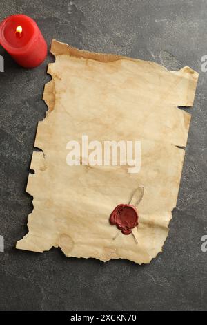 Blatt altes Pergamentpapier mit Wachsstempel und Kerze auf grauem Tisch, Draufsicht Stockfoto