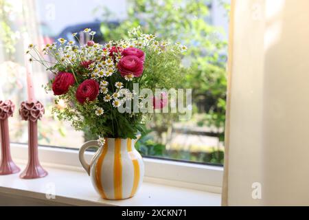 Wunderschöne Ranunkelblumen und Kamillen in Vase auf Fensterbank drinnen Stockfoto