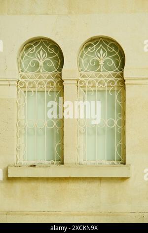 Zwei Fenster mit einem weißen Rahmen und einem grünen Vorhang. Die Fenster sind gewölbt und haben ein dekoratives Design Stockfoto