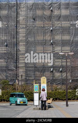 Eine ältere Japanerin überprüft den Fahrplan an einer Bushaltestelle in Tsukimino, hinter der ein Appartementgebäude repariert wird. Kanagawa. Japan. Stockfoto