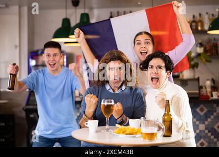 Eine Gruppe von emotionalen Freunden, die die Lieblingsmannschaft mit der Flagge Frankreichs anfeuern, während sie das Spiel in der Bar im Fernsehen anschauen Stockfoto