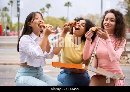 Drei Frauen sitzen auf einer Bank und essen Pizza Stockfoto