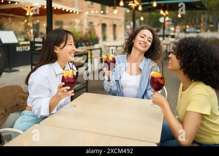 Drei Frauen sitzen an einem Tisch mit Drinks und Lächeln Stockfoto