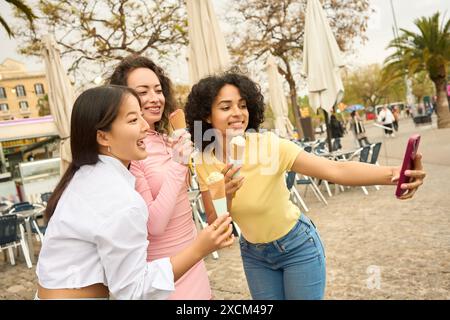 Drei junge Frauen genießen Eis und nehmen Selfies Stockfoto