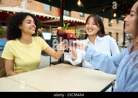 Drei Frauen sitzen an einem Tisch, jede hält ein Glas Wein Stockfoto