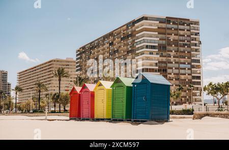 Bunte Strandhütten mit hohen Wohngebäuden und Palmen im Hintergrund schaffen eine lebhafte Küstenlandschaft. Strand Sant Antoni, Cullera, Spanien Stockfoto