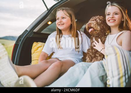 Kleine Mädchen, die mit einem flauschigen braunen Maltipoo-Hund spielen, während du im Kofferraum sitzt. Sie spielen mit dem Hund und schaffen eine fröhliche und lebendige Szene während des Auto Stockfoto