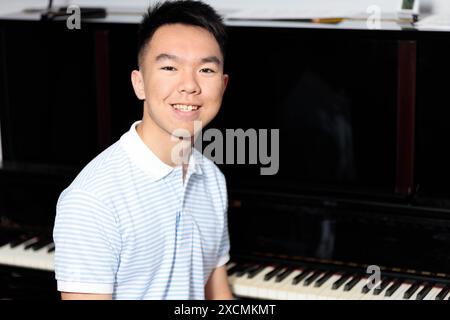 Ein asiatischer Teenager sitzt glücklich an einem Klavier in seinem Haus und blickt direkt in die Kamera mit einem Lächeln im Gesicht, um ein Porträt zu erhalten. Stockfoto