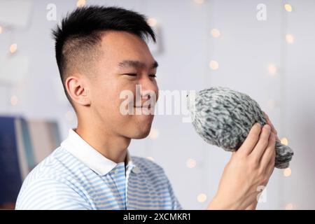 Ein männlicher Teenager lächelt, während er ein Plüschtier in seinem Schlafzimmer hält Stockfoto