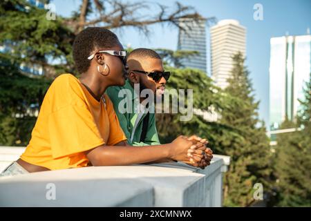 Friedliches afroamerikanisches Paar im Park, lehnt sich an einen Zaun und blickt nachdenklich in die Ferne. Stockfoto