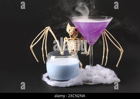 Gläser köstlicher Cocktails mit gruseligen Skelett auf schwarzem Hintergrund. Halloween-Konzept Stockfoto