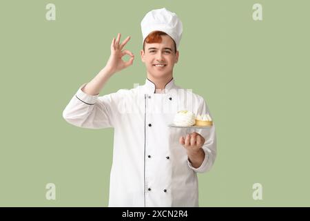 Männliche Konditorin in einheitlichem Stand mit leckeren Desserts und OK-Geste auf grünem Hintergrund Stockfoto
