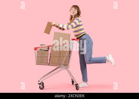 Eine junge Frau mit einem Einkaufswagen voller Pappschachteln auf rosa Hintergrund Stockfoto