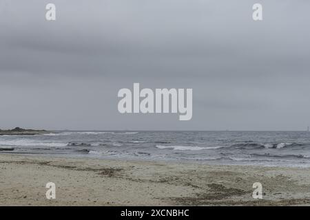 Ein friedlicher Blick auf den Strand Punta Prima auf Menorca, mit einem Sandstrand, sanften Wellen und einem fernen Segelboot unter einem bewölkten Himmel. Stockfoto