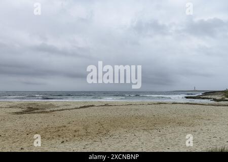 Ein friedlicher Blick auf den Strand Punta Prima auf Menorca, mit einem Sandstrand, sanften Wellen und einem fernen Segelboot unter einem bewölkten Himmel. Stockfoto