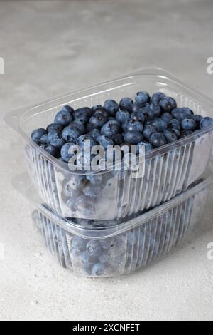 Frische Heidelbeeren in Plastikbehältern auf grauem Hintergrund, Beeren zum Einfrieren vorbereiten Stockfoto