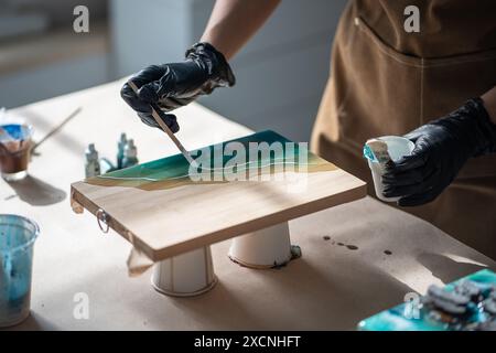 Die Hände einer sorgfältigen Künstlerin arbeiten Details der Malerei aus und schaffen Kunstwerke aus Epoxidharz. Stockfoto