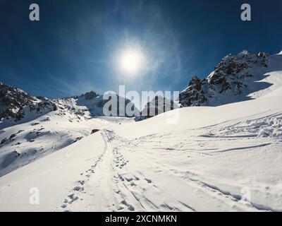 Atemberaubende Winterlandschaft eines gefrorenen Berges mit der Sonne, die durch die Wolken bricht - ein Bergsteigerweg, der sich durch das schneebedeckte Gelände schlängelt Stockfoto