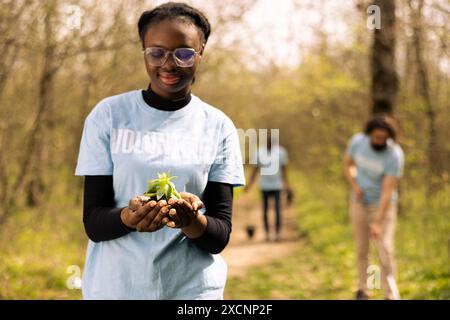 afroamerikanischer junger Aktivist, der einen kleinen Pflanzenspross mit organischem Boden hält und sich für den Erhalt der Natur und des Waldökosystems einsetzt. Stolzes Mädchen, das freiwillig dafür arbeitet, Bäume anzubauen. Stockfoto