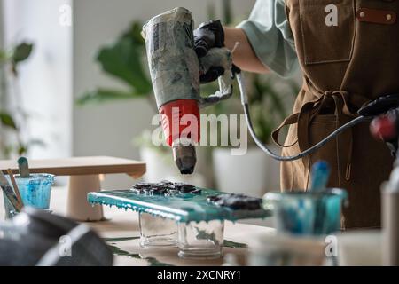 Professionelle Frauenhände arbeiten mit Epoxidharz, um Meisterwerke auf Leinwand mit Flüssigkeit zu erschaffen. Stockfoto