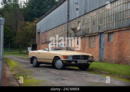 Gelbes Mercedes Benz 450SL Cabriolet auf einer Fahrbahn bei einem alten Fabrikgebäude Stockfoto