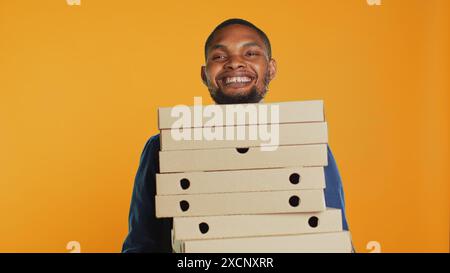 Der Pizzeria-Kurier in Afrika bringt Pizzakästen für Expresszustellung mit und gibt dem Kunden Lebensmittel. Ein freundlicher Mitarbeiter für den Take-out-Service hält ein Essen-Paket zum Mitnehmen bereit. Kamera A.. Stockfoto