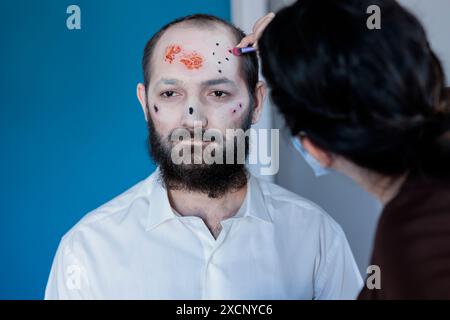 Die Frau hilft dem Mann, sich auf halloween vorzubereiten, kleidet ihn als einen furchterregenden Zombie an. Eine Frau, die falsche Blutwunden und Narben auf den Ehemann aufträgt und ihn in eine Horrorkreatur verwandelt Stockfoto