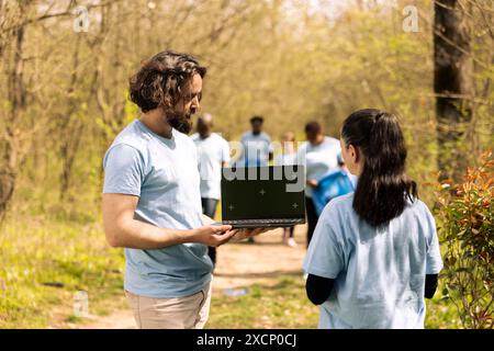 Ein Team von Freiwilligen aus ökologischem Bereich nutzt pc mit Grünschirm im Wald, um Müll zu sammeln und Bäume für zukünftige Generationen zu Pflanzen. Umweltschutz des natürlichen Lebensraums. Stockfoto