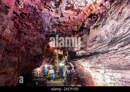 Der Lavatunnel (Raufarholshellir) in Island, Innenansicht der Lavatunnel mit roten vulkanischen Felsformationen, Metallsteg und Touristen. Stockfoto