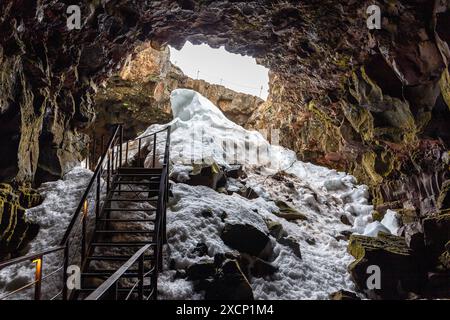 Der Lavatunnel (Raufarholshellir) in Island, Innenansicht des Eingangs zur Lavaröhre mit eingestürzter Decke, Metallsteg und Schnee. Stockfoto