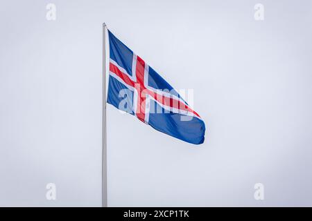 Die isländische Nationalflagge mit rotem und weißem Kreuz auf blauem Hintergrund, die im Wind vor blauem Himmel fliegt. Stockfoto