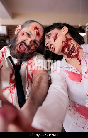 Schauspieler, die Spaß in Office-Horrorfilmen haben, verkleidet als Zombies, machen Selfies. Mann und Frau, die mit falschen Wunden bedeckt sind, spielen in Thriller-Filmen, die hinter den Kulissen Aufnahmen, POV Stockfoto