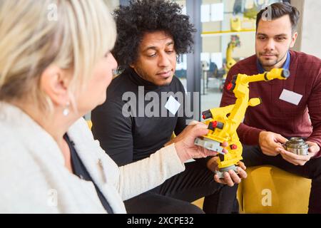 Team aus verschiedenen Fachleuten, die einen Roboterarm-Prototyp untersuchen und diskutieren, der für den Einsatz in der industriellen Automatisierung und Fertigung entwickelt wurde. Stockfoto