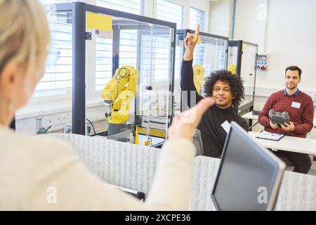 Vielfältige Gruppe von Fachleuten in einer industriellen Schulung, die über Robotik und Prozessautomatisierung lernen, mit Robotergreifern hinten Stockfoto