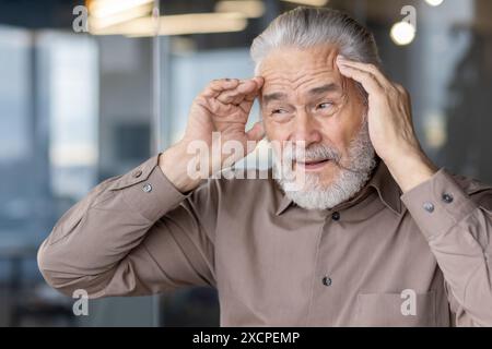 Älterer Mann mit Kopfschmerzen und Kopfschmerzen. Reifer Mann im Stress, der seine Schläfe hält. Ein älterer Mann leidet unter Unannehmlichkeiten, wenn er drinnen ist. Stockfoto