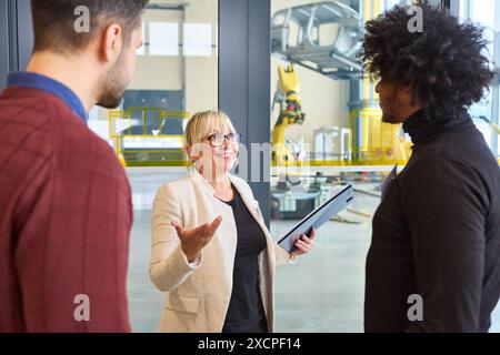 Drei Personen diskutieren Robotik und Automatisierung in einem industriellen Umfeld. Technologische Innovation, Teamwork und Engineering sind die wichtigsten Konzepte. Stockfoto