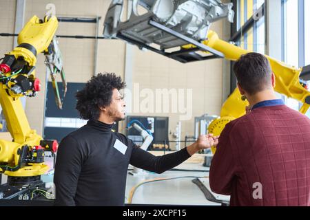 Ingenieure diskutieren die Funktion und Anwendung eines Industrieroboters mit Greifarm, der in der Automobilproduktion in einem modernen Fabrikgebäude eingesetzt wird Stockfoto