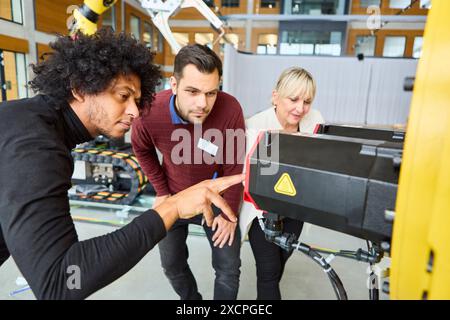 Gruppe von Ingenieuren, die gemeinsam an der Programmierung und Inspektion eines Roboterarms arbeiten und sich auf industrielle Automatisierung und technologische Fortschritte konzentrieren. Stockfoto