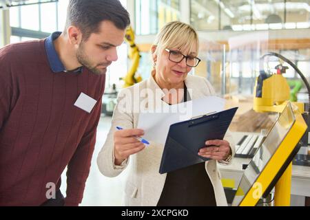 Zwei Ingenieure prüfen Dokumente und diskutieren Robotik-Programmierung in einem industriellen Umfeld mit Schwerpunkt auf Automatisierungs- und Produktionsanwendungen. Stockfoto