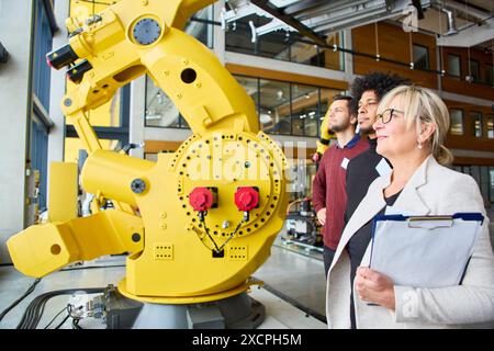 Gruppe von Ingenieuren, die einen Industrieroboter mit Greifarm in einem modernen Arbeitsbereich diskutieren und sich auf Robotik-Schulungen und -Programmierung für verschiedene i konzentrieren Stockfoto