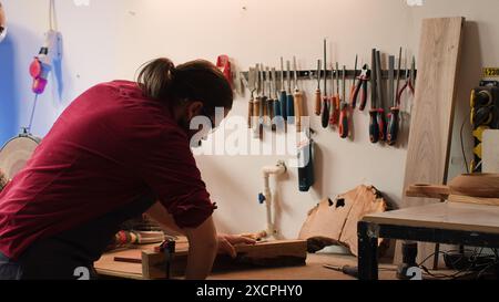 Holzarbeiter mit einem Schraubstock zum Halten des Holzblocks und Beginn der Möbelmontage in der Werkstatt. Handwerker in der Tischlerei mit einem Schraubstock, um ein Stück Holz zu spannen, bevor es geschnitzt wird, Kamera A Stockfoto