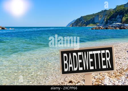 Deutschland, Bayern - 18. Juni 2024: Badewetter - steht auf einem Schild an einem sonnigen Strand mit Wasser vor dem Meer. Konzept Baden und Schwimmen bei hohen Temperaturen oder Hitze und Sommerwetter. FOTOMONTAGE *** Badewetter - stehen auf einem Schild an einem sonnigen Strand mit Wasser vor dem Meer. Konzept Baden und schwimmen bei hohen Temperaturen, bzw. Hitze und sommerlichen Wetter. FOTOMONTAGE Stockfoto