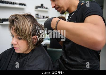 Professioneller Friseur, der in einem modernen Schönheitssalon Farbakzente auf das Haar einer Frau aufträgt. Der Kunde erhält eine Haarbehandlung mit Schwerpunkt auf Haarpflege Stockfoto