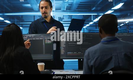 Manager und IT-Supportspezialisten arbeiten zusammen und überwachen Serverzeilen im Rechenzentrum für Netzwerksicherheit. Supervisor und Mitarbeiter aus mehreren ethnischen Gruppen, die Supercomputer beaufsichtigen Stockfoto