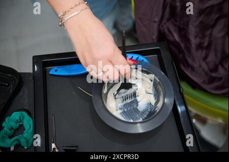 Die Hand des Friseurs bereitet in einem Schönheitssalon Haarfärbemittel in einer Schüssel mit einer Bürste vor. Wichtige Salonwerkzeuge sind auf dem Tisch sichtbar. Stockfoto